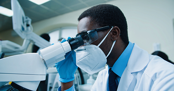Scientist wearing mask looking into microscope