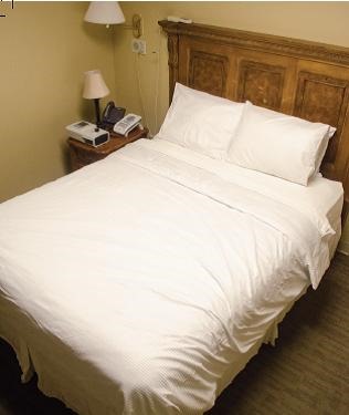 A neatly made bed with white linens and pillows sits in a bedroom-style sleep study room next to a bedside table with monitoring equipment